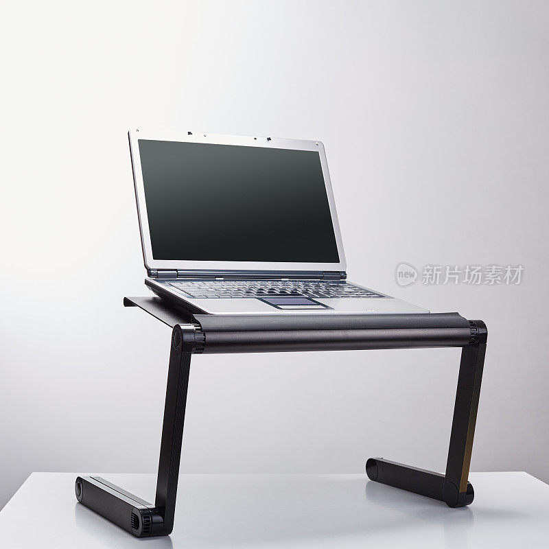 Laptop computer sits on a portable holder riser or stand against white background